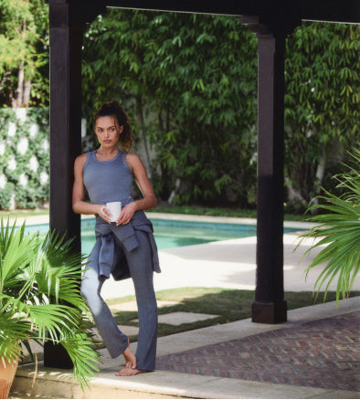 Woman in a blue outfit standing by a pool with greenery in the background